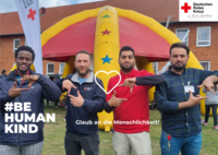 Foto von vier Männern auf einem DRK-Fest. Auf dem Bild steht der Text "Glaub an die Menschlichkeit!" und "#BEHUMANKIND". Zwischen den Männern ist ein weißes Herz gezeichnet.