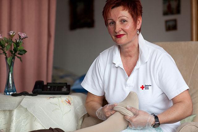 Eine DRK Mitarbeiterin aus dem Pflegebereich zieht einer anderen Person Strümpfe an.