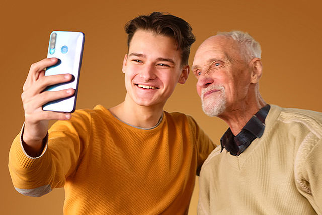 Ein junger Mann und sein Opa machen lächelnd ein Foto von sich.
