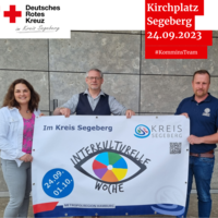Drei Menschen halten ein Banner der Interkulturellen Woche Bad Segeberg.