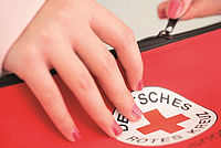 Eine Hand öffnet den Reisverschluss einer Tasche mit dem DRK Logo.