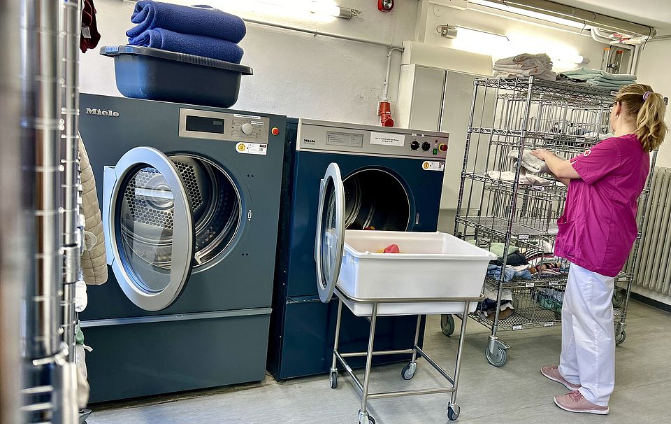 Hauswirtschaft WuP DRK Mitarbeiter steht mit Kleidung in der Hand vor einer Waschmaschine.