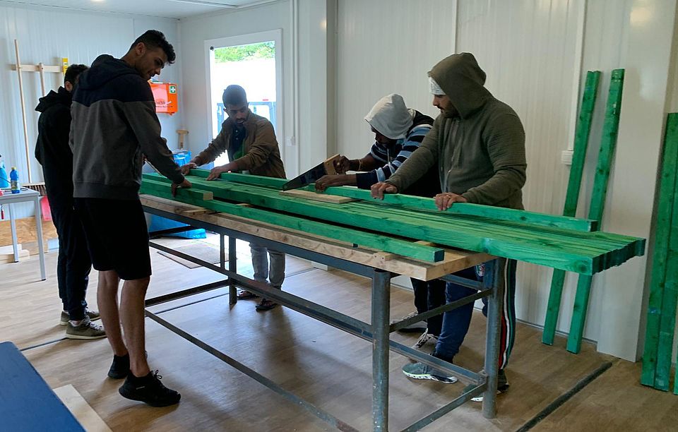 Fünf Männer zersägen große Balken von grünem Holz in der Holzwerkstatt.