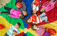 Kinder liegen auf einem bunten Tuch und spielen mit DRK Luftballons.
