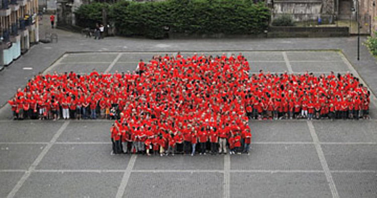 Das Deutsche Rote Kreuz Symbol wird abgebildet durch viele Ehrenamtler, die rote T-Shirts tragen und in der Form eines Kreuzes beieinander stehen.