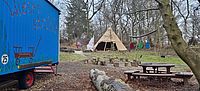 Außenbereich der DRK Kita Wiesenstrolche. Ein Tisch, Holzsitze, ein Zirkuswagen und ein Stoffzelt stehen auf einer Wiese.