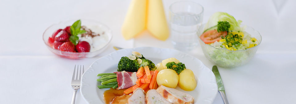 Verpfelgung Gedeckter Tisch mit einer Schale Salat, einem vollen Hauptspeisen-Teller und einem Nachtisch.