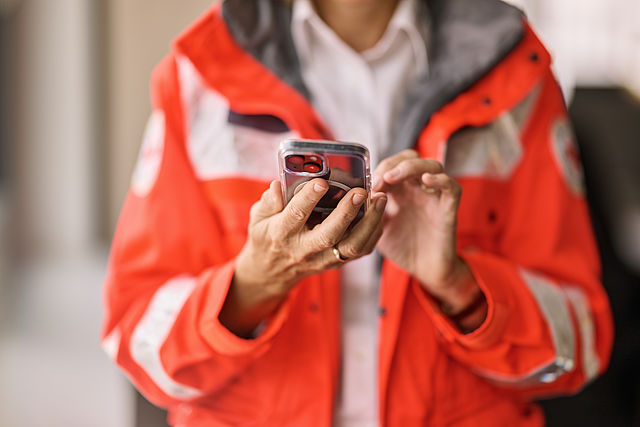 Person in DRK Kleidung hält ein Smartphone in der Hand.