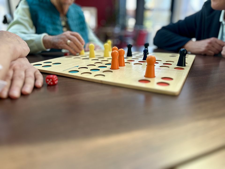 Spiele WuP Spielbrett steht zwischen drei älteren Personen.
