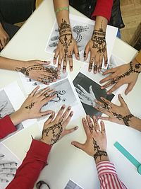 Acht Hände liegen in einem Kreis auf einem Tisch. Alle Hände wurden vorher mit Henna individuell bemalt.