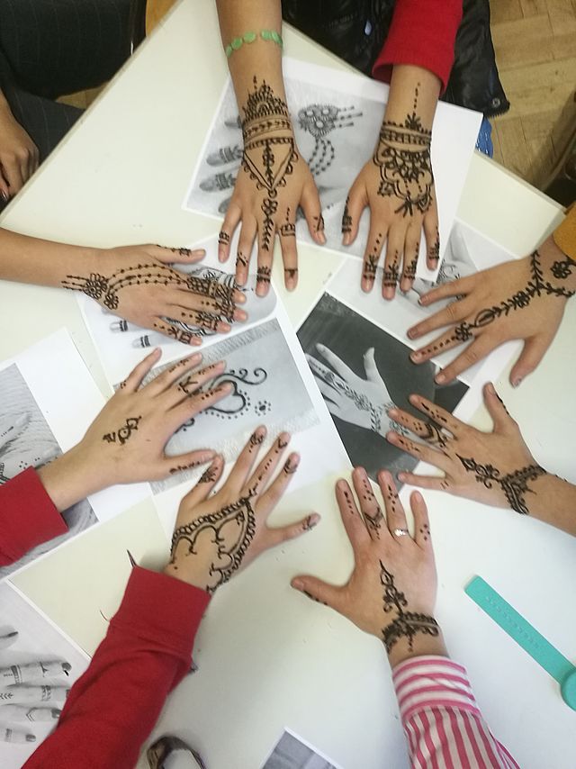 Acht Hände liegen in einem Kreis auf einem Tisch. Alle Hände wurden vorher mit Henna individuell bemalt.