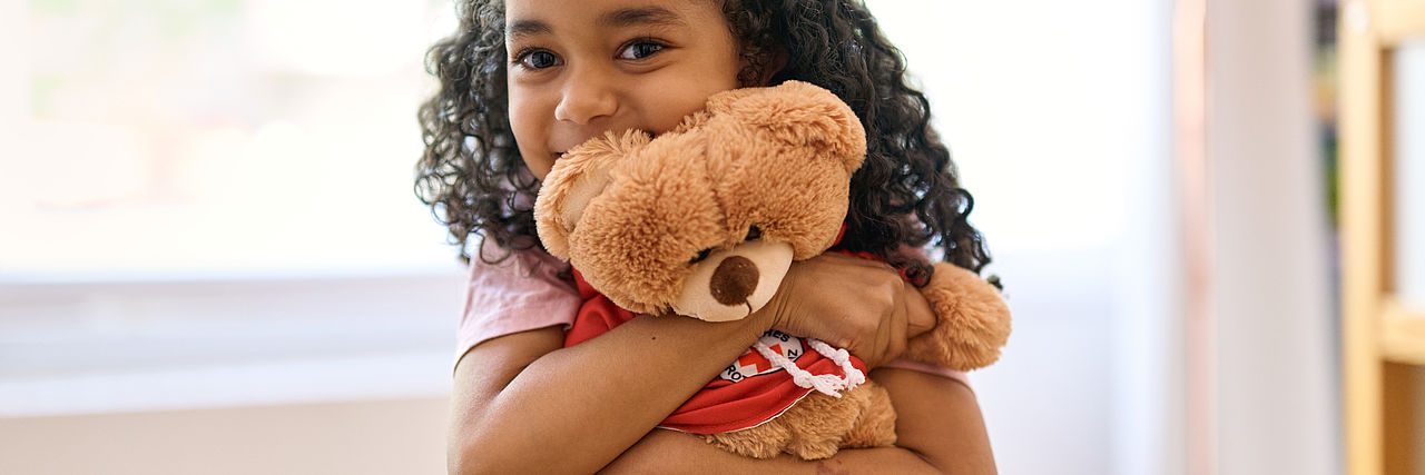 Mädchen hält einen Teddybären im Arm.